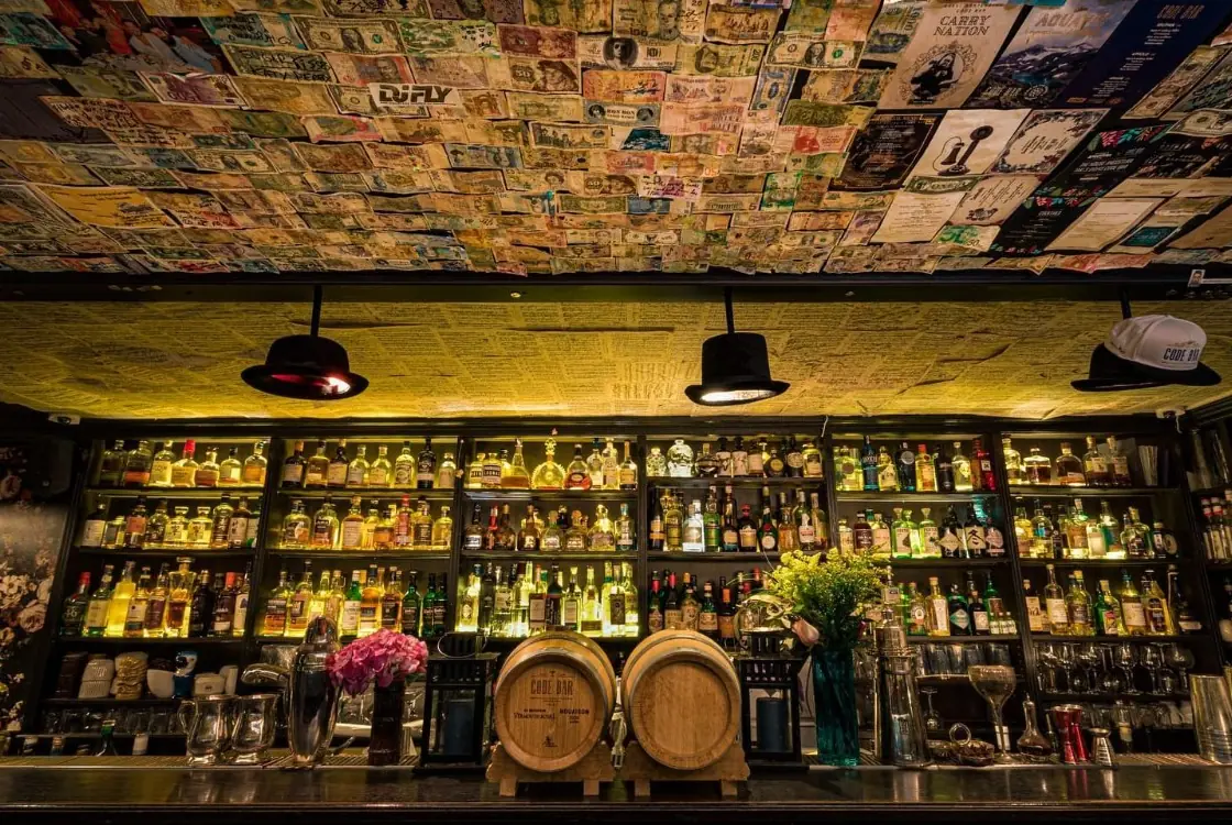 Le mur de bouteilles du Code Bar, ses fûts et son plafond couvert de billets